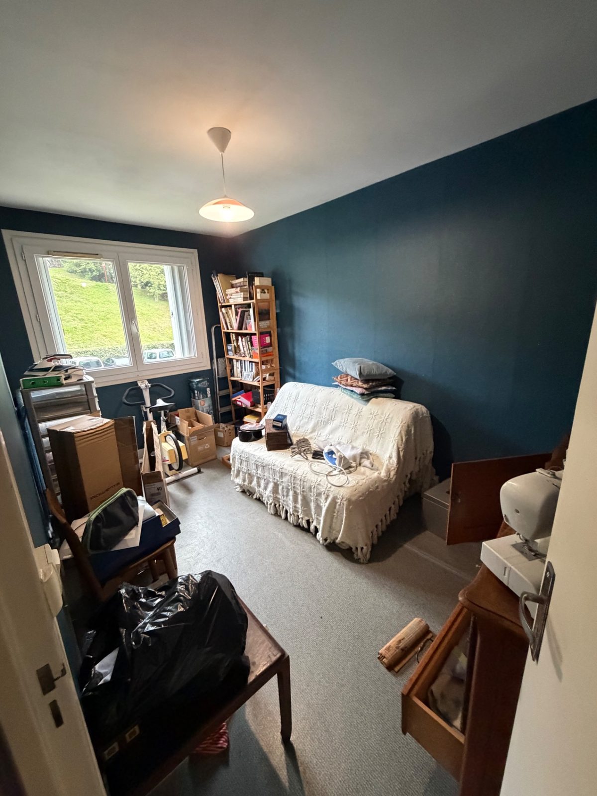 Chambre aux murs bleus encombrée de cartons, d'un canapé-lit et de petits meubles avant débarras à Béhobie