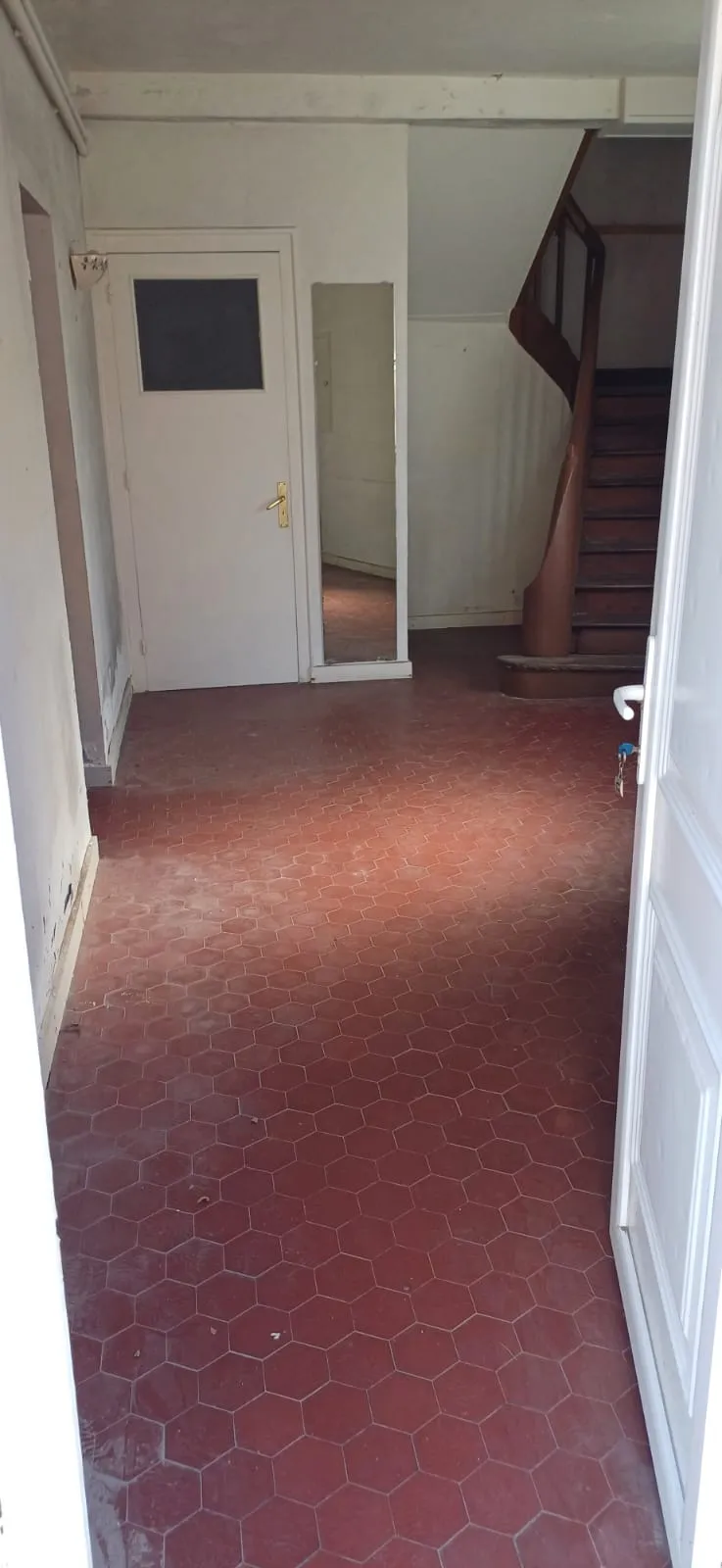 Entrée vide avec dalles hexagonales rouges et escalier en bois, après débarras
