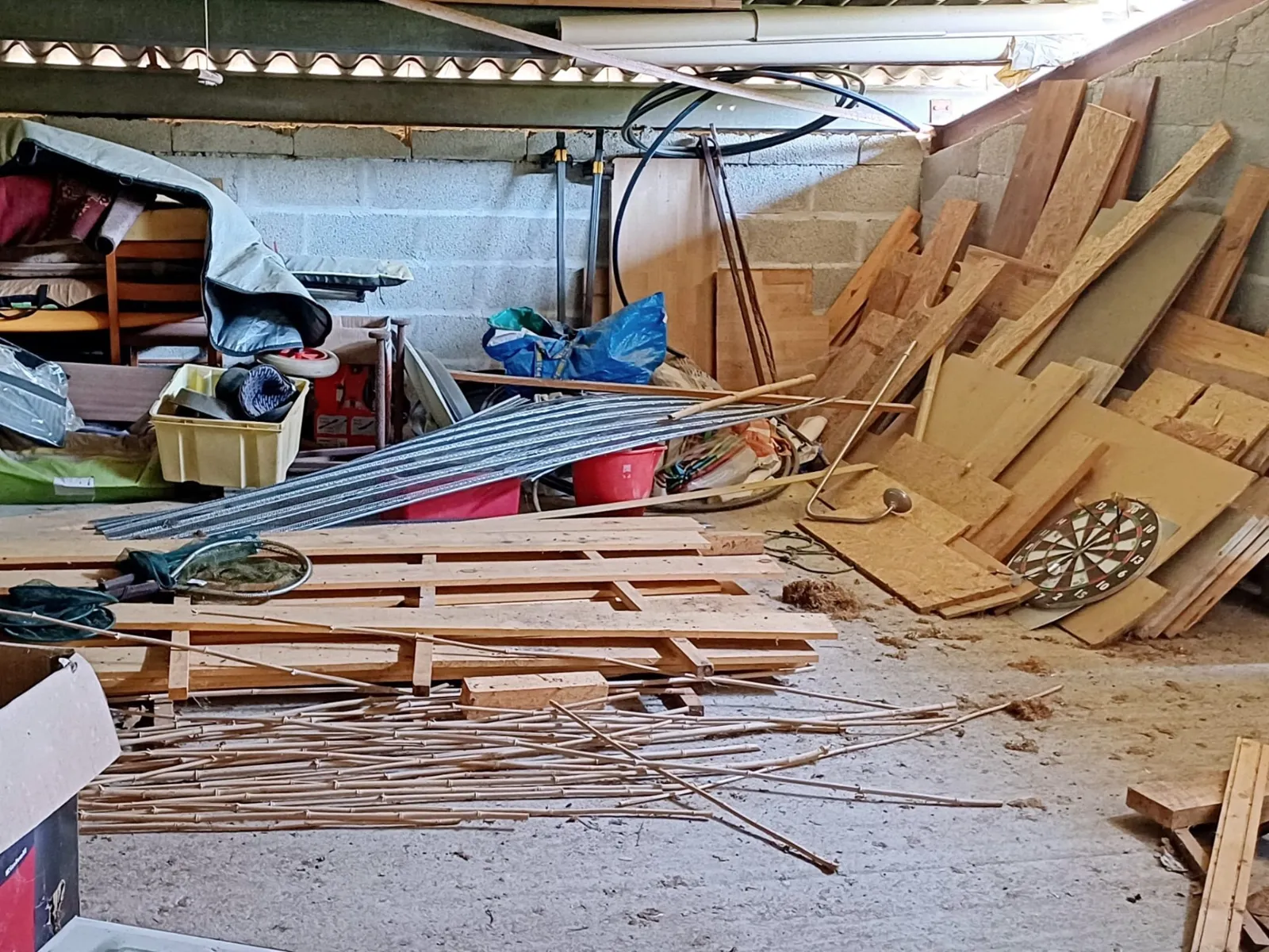 Dépendance encombrée de planches, chutes de bois et bacs, avant débarras