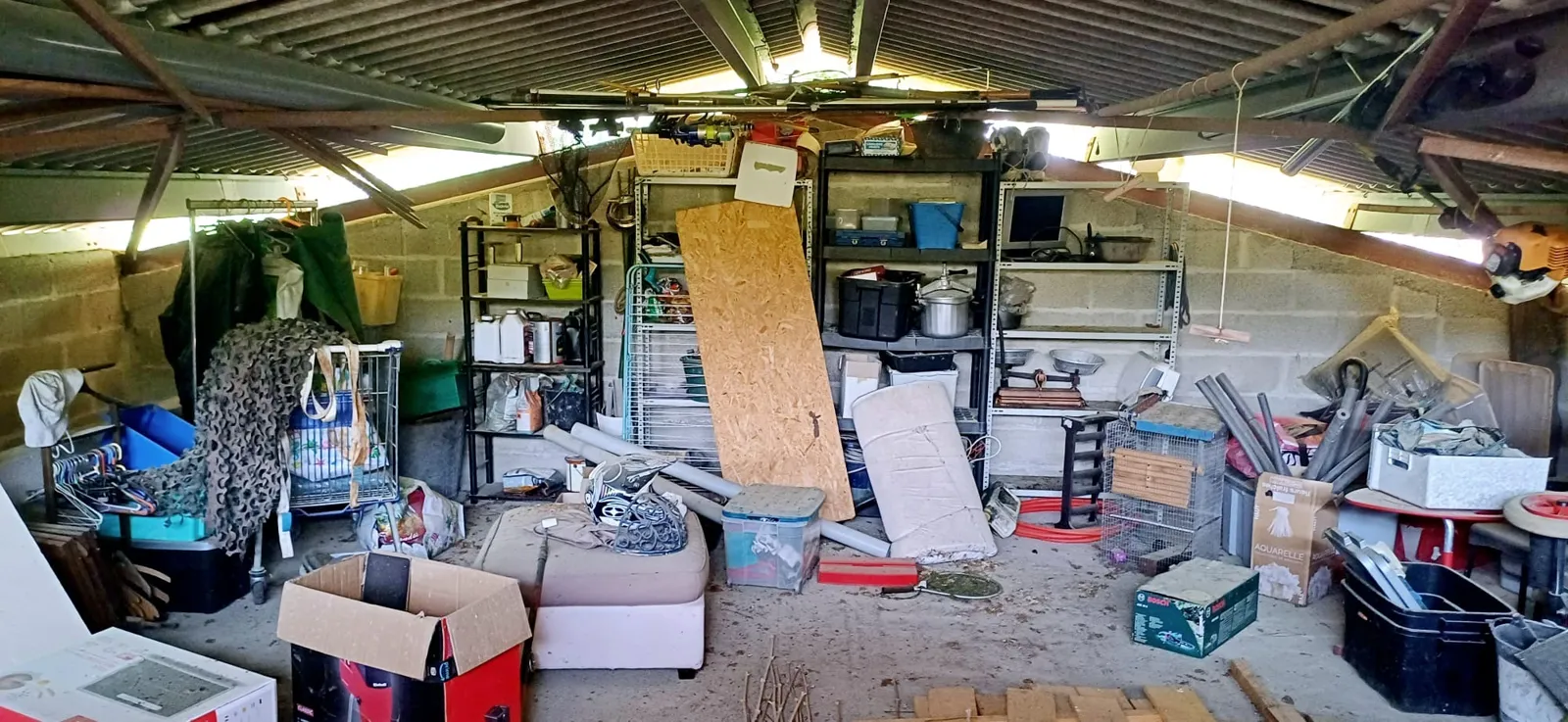 Garage encombré d'étagères, cartons, bacs et matelas, avant débarras