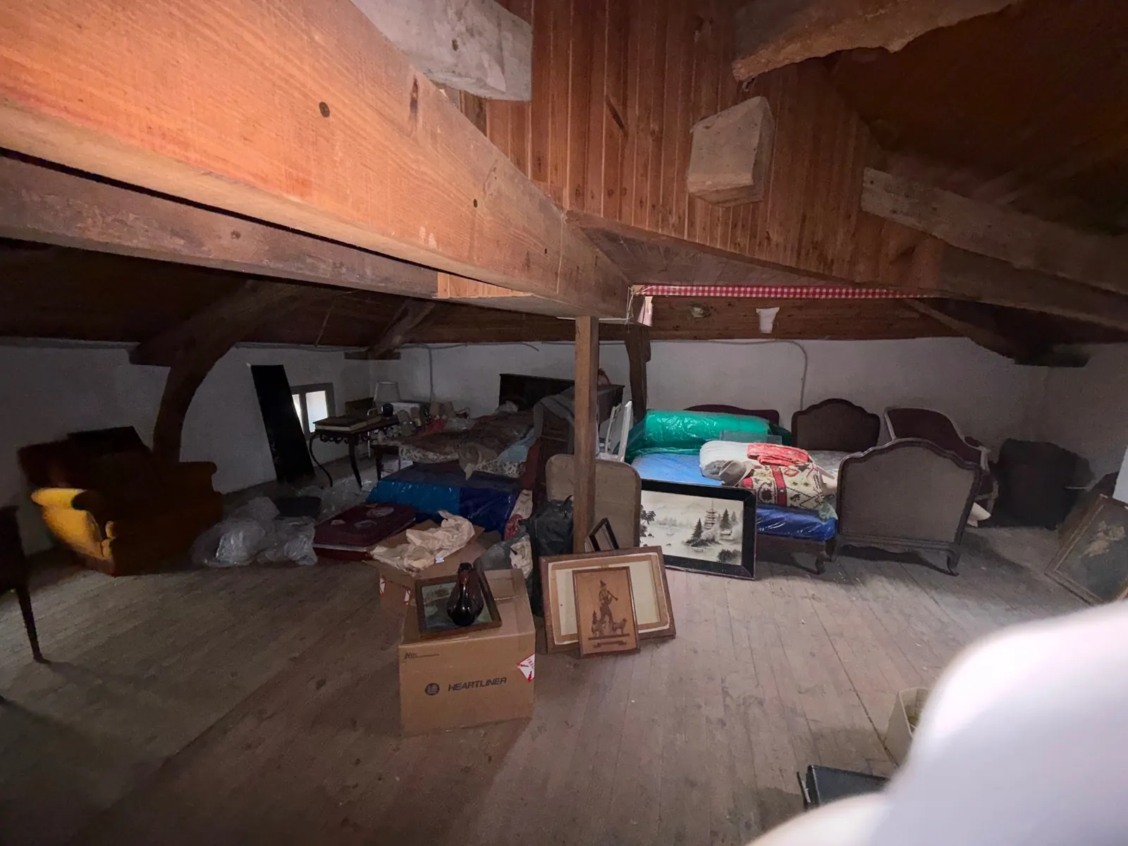 Grenier encombré de lits, fauteuils, cartons et meubles sous les poutres, avant débarras