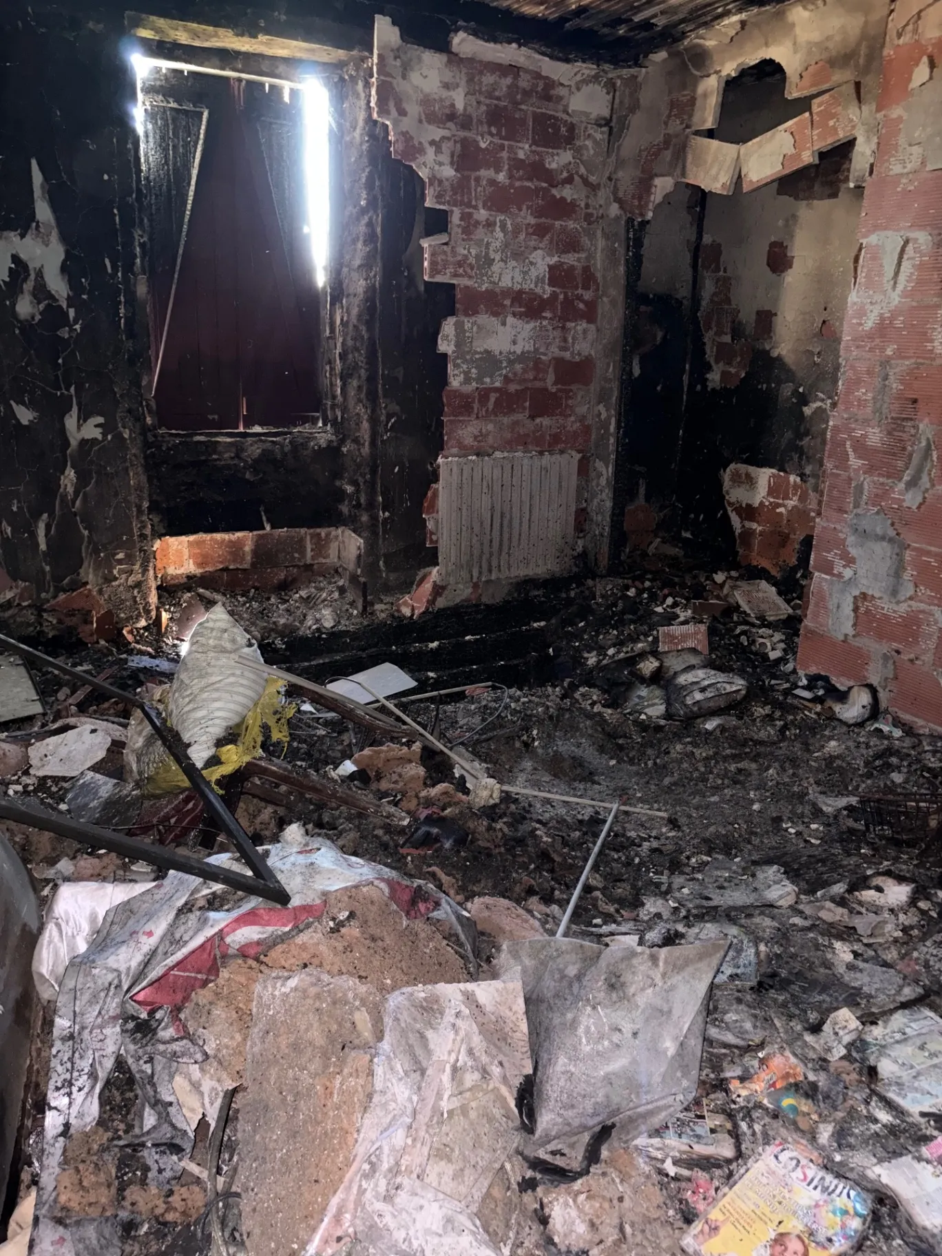 Pièce incendiée aux murs noircis et briques à nu, gravats au sol, avant débarras