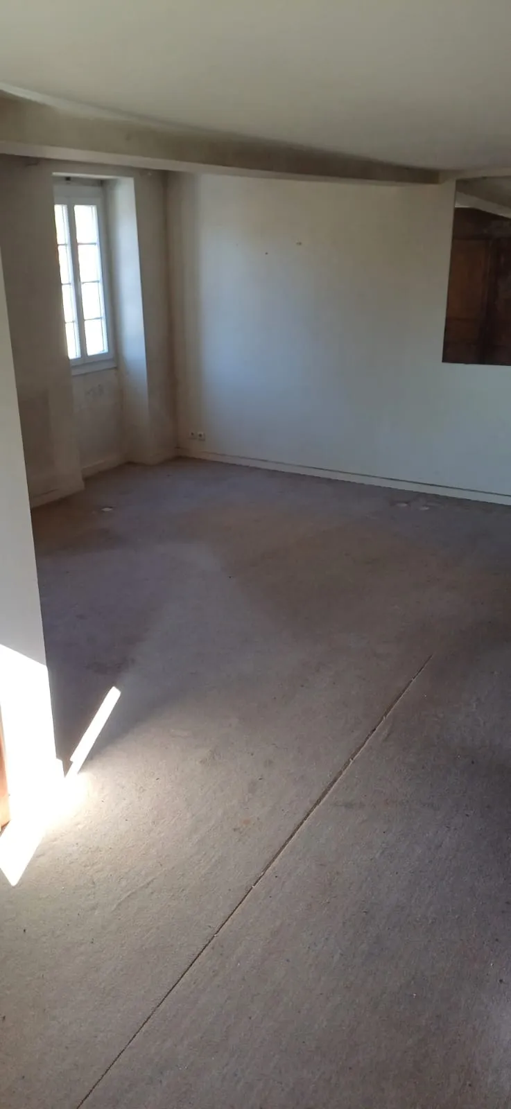 Pièce vide avec moquette, poutre et fenêtre à petits carreaux, après débarras