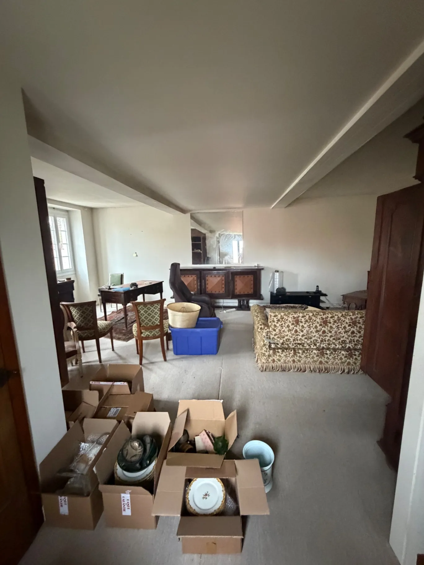 Grand séjour avec bureau, canapé, buffet et cartons de vaisselle, avant débarras