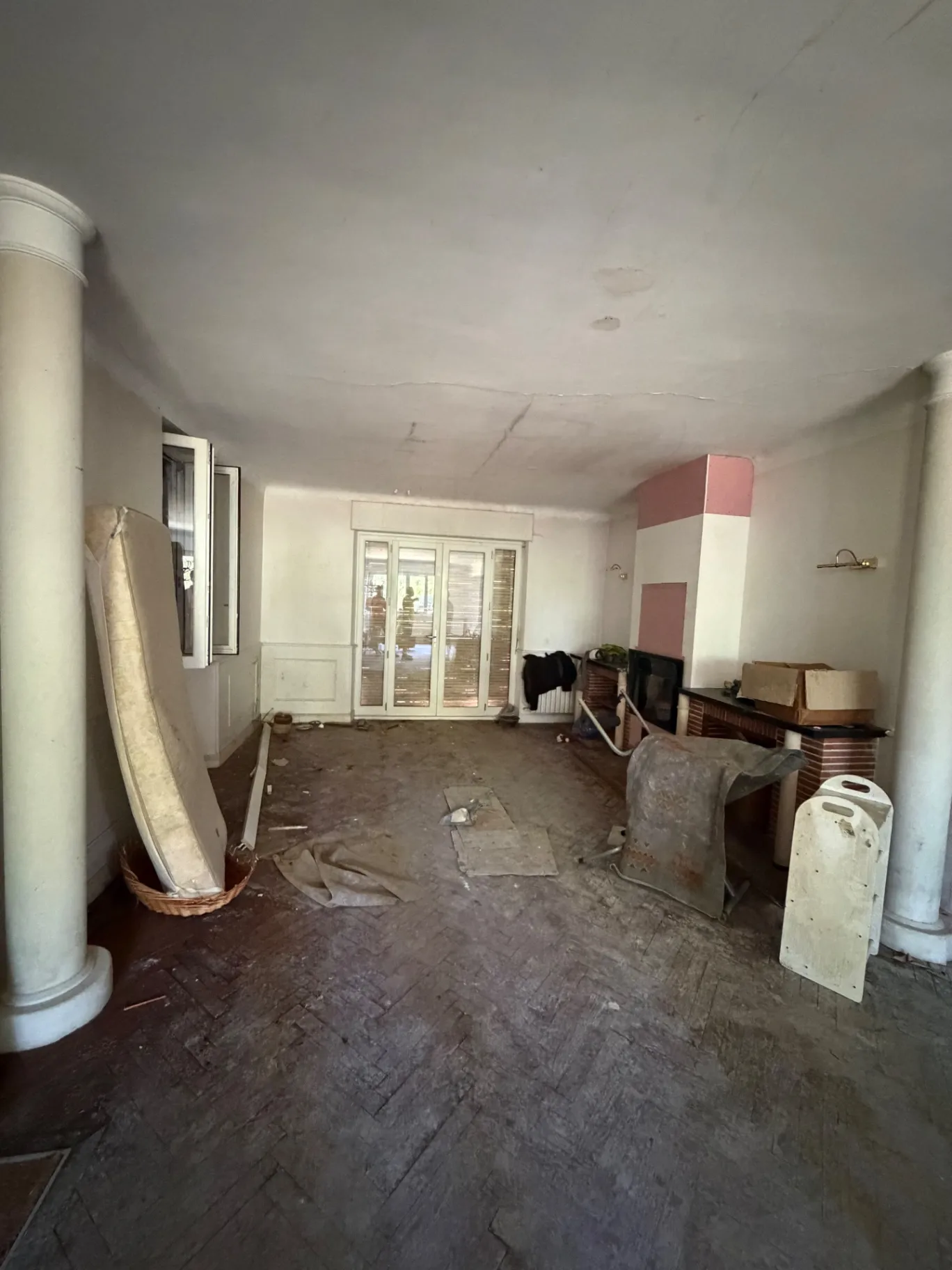 Séjour à colonnes avec matelas, tapis et débris sur parquet, avant débarras